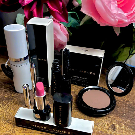 Elegant Marc Jacobs 6-piece luxury beauty gift collection featuring a glossy compact omega eyeshadow in the color “oh Boy”, A Limited Edition Signature Coconut Setting Spray, The Famous Award winning Highliner Gel Eye Crayon in the color “Blacquar” and an assortment of matching designer beauty cosmetics, complemented by a backdrop of lush pink, green & white florals.