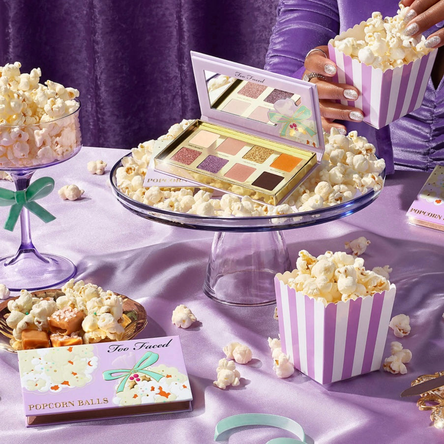 Too faced eyeshadow palette sitting in a bowl of popcorn on a table full of popcorn kernels 