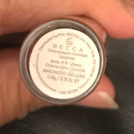 This Lip Gloss Is A very warm-toned, light-medium Tan (Soft Brown) with a hint of Peach pearl finish. It is a sheer lip-gloss that not sticky and goes on smooth and with ease. The 3D light-reflecting pigments as well as Ginger, Peppermint oil, and a non-stinging peptide make lips appear fuller and smoother. Contains Vitamins C and Vitamin E, plus hydrating Shea Butter and Muru Muru Butters to soften, protect and condition the lips. Becca Champagne Cocktail Lip Gloss shade "Bellini"